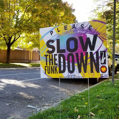A colorful yard sign with the text "Slow the Funk Down!" and facing the street in someone's yard