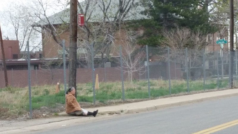 Woman sits on the sidewalk at bus stop in Globeville