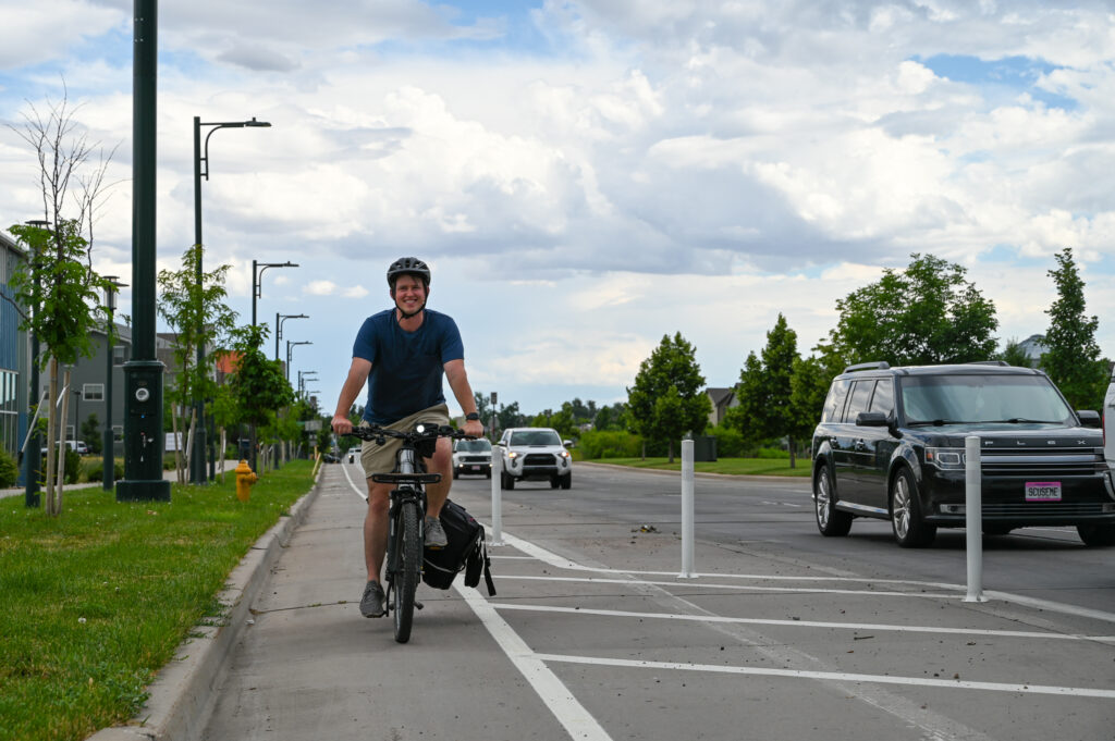 A bicyclist approaches an intersection in the protected bike lane with a bulb out between them and the cars on the road to their left.
