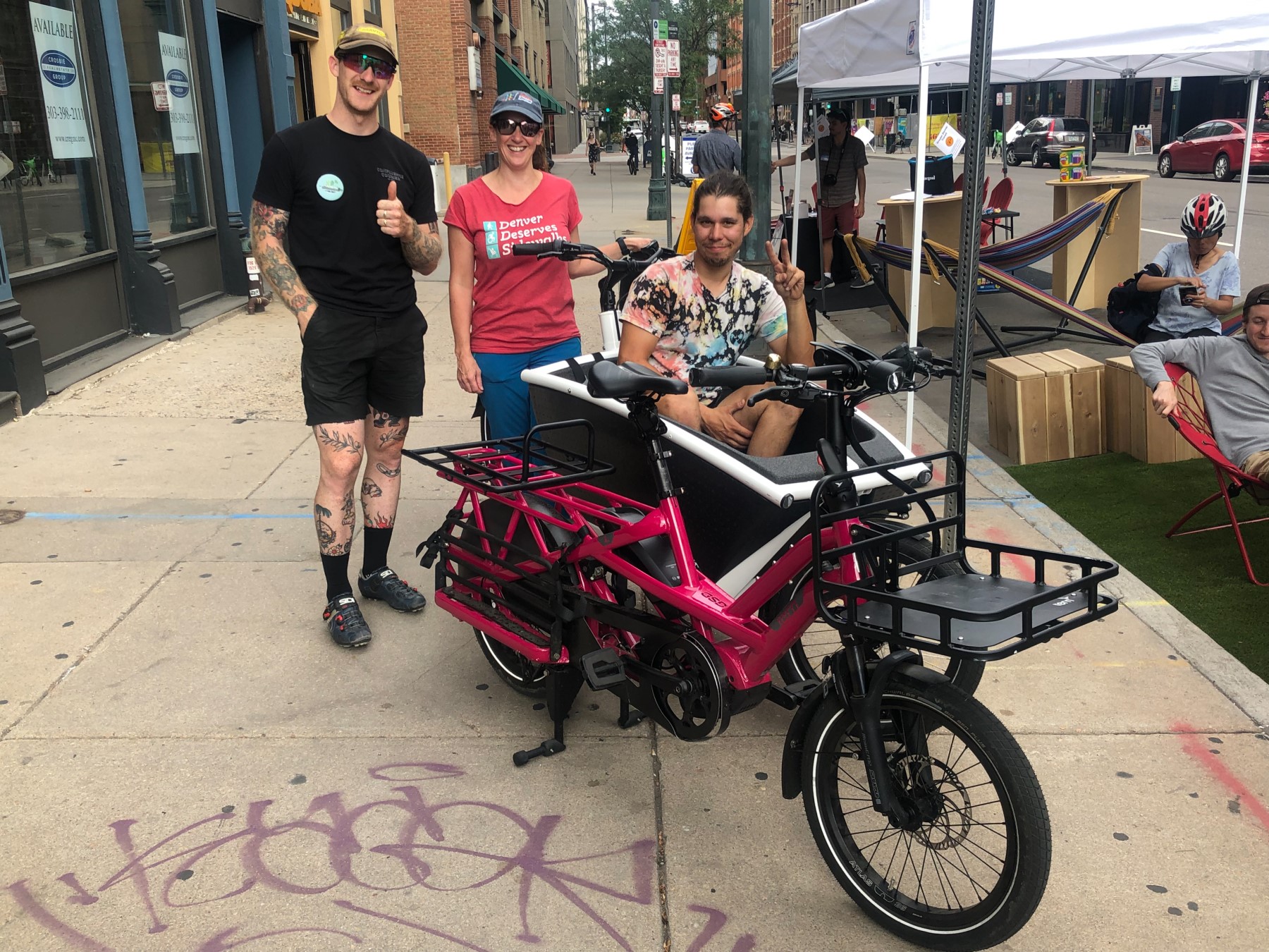 Three people stand with a front loading eCargo bike and a pink eCargo bike with rear cargo space.