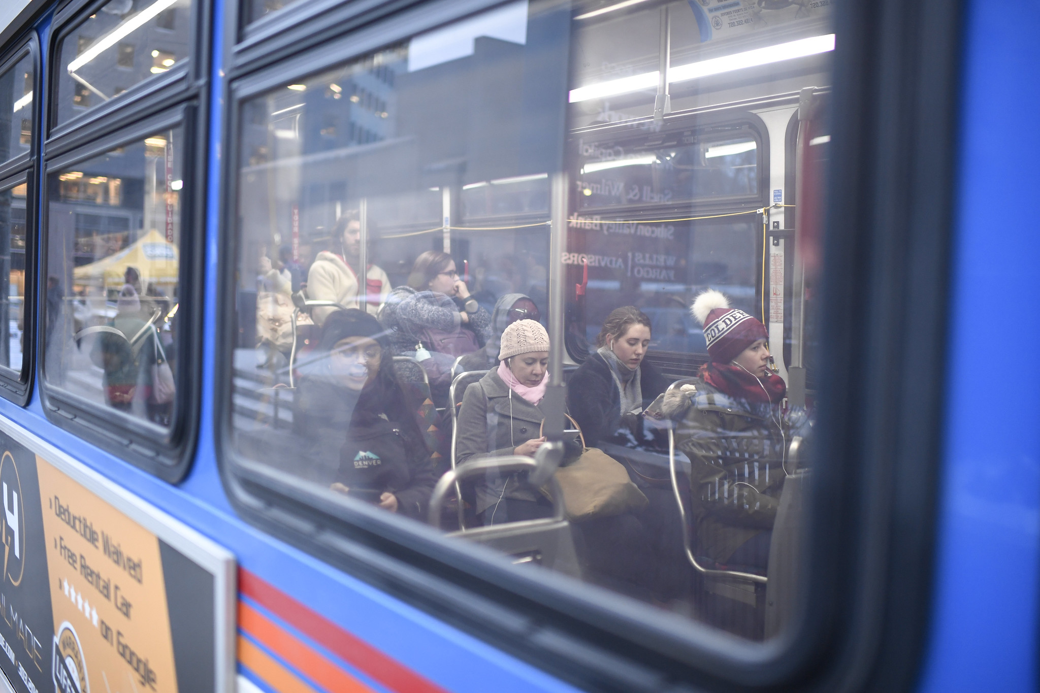 A shot from the outside looking into the window of a bus with people sitting inside.