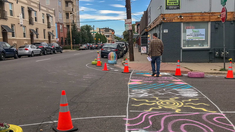 A sidewalk drawn in chalk with colorful designs and cones marking a bulbout on 13th Avenue.