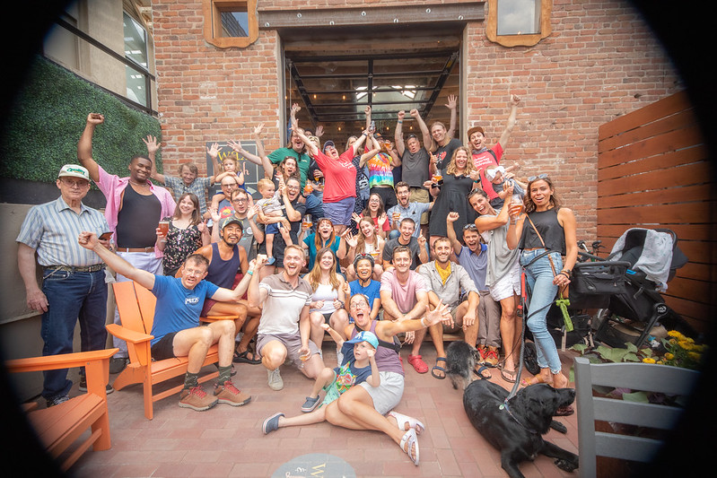 A group of about 40 people and kids cheer together and smile big for the camera on a public patio.