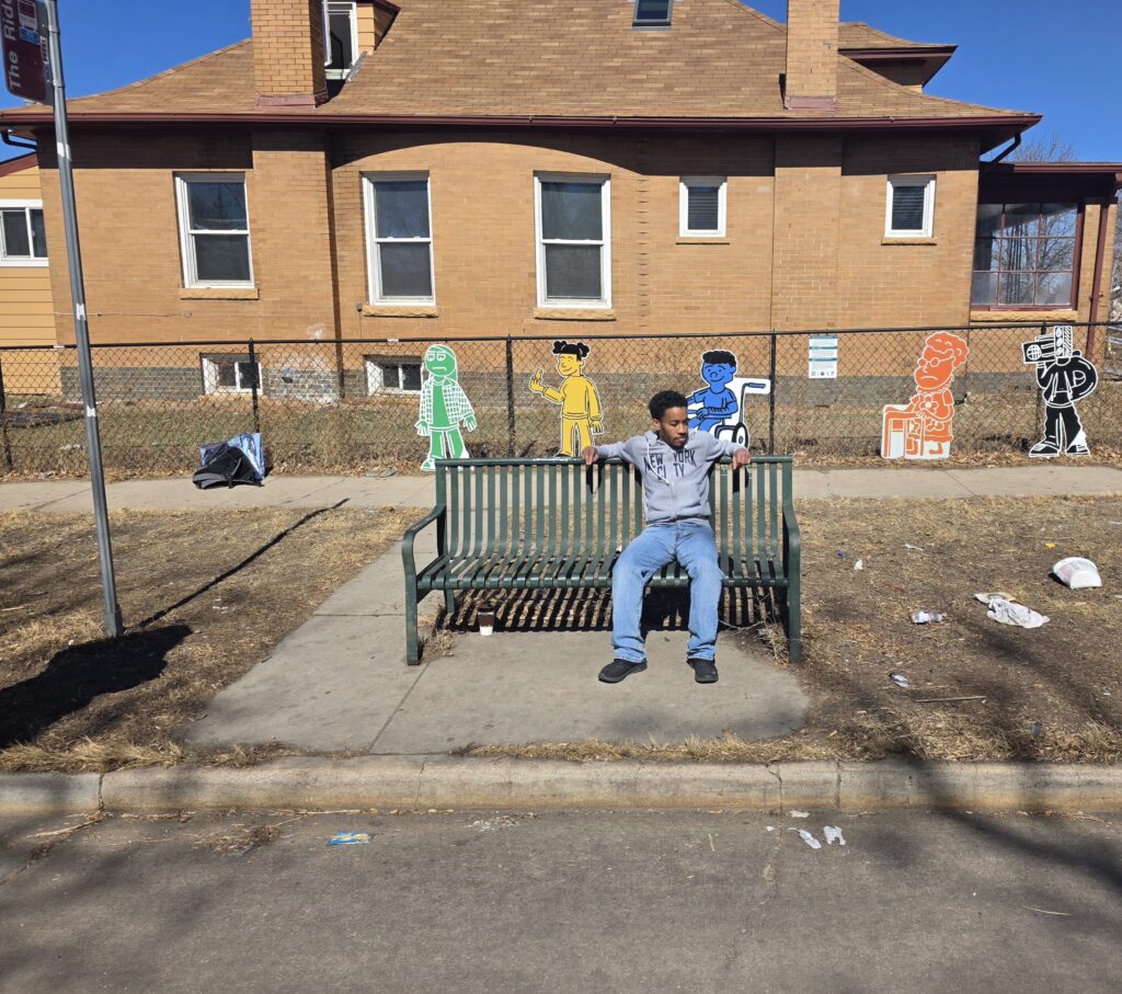 Artist AJ Kiel sits in front of his art piece installed at MLK Jr Boulevard and York Street