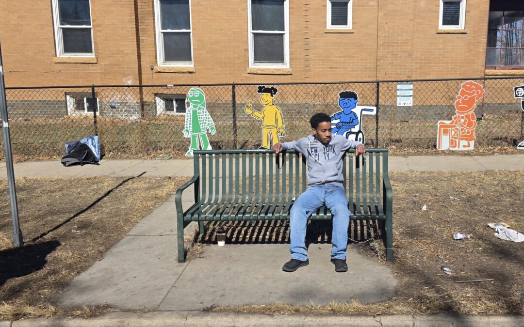 Artist AJ Kiel sits in front of his art piece installed at MLK Jr Boulevard and York Street