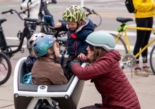 Mom crouching down next to a cargo bike carrying two small kids